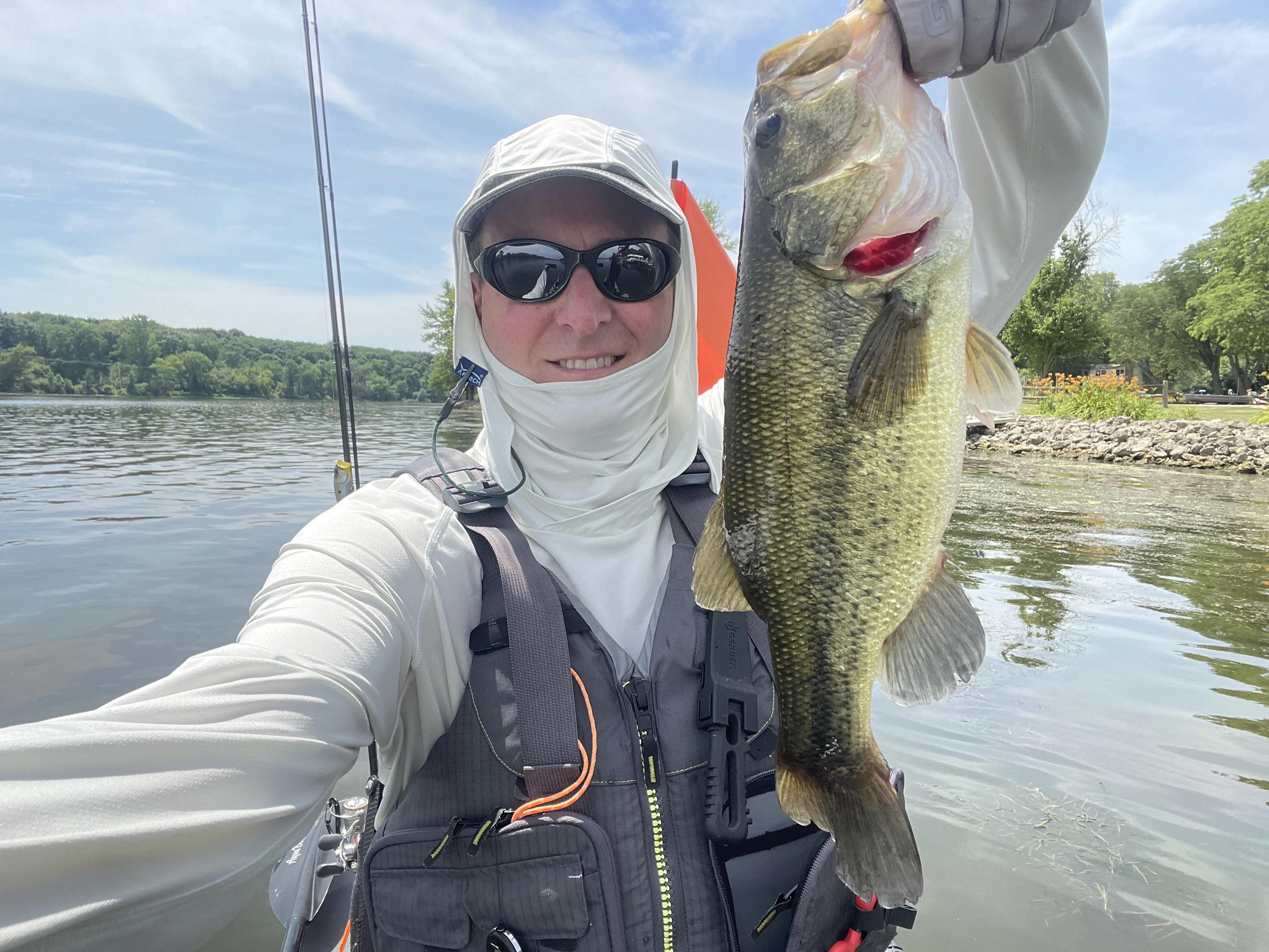 Tyler holding a largemouth bass beside a riprapped shoreline